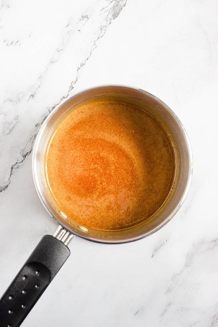 A saucepan with melted browned butter on a white marble surface, ready to make rich Caramel Sauce for dipping freshly baked Air Fryer Churro Donut Holes.