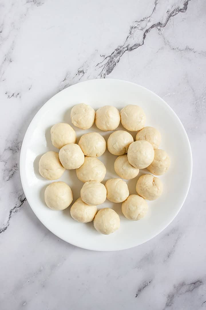 A white plate with 20 small, round dough balls on a white marble surface.