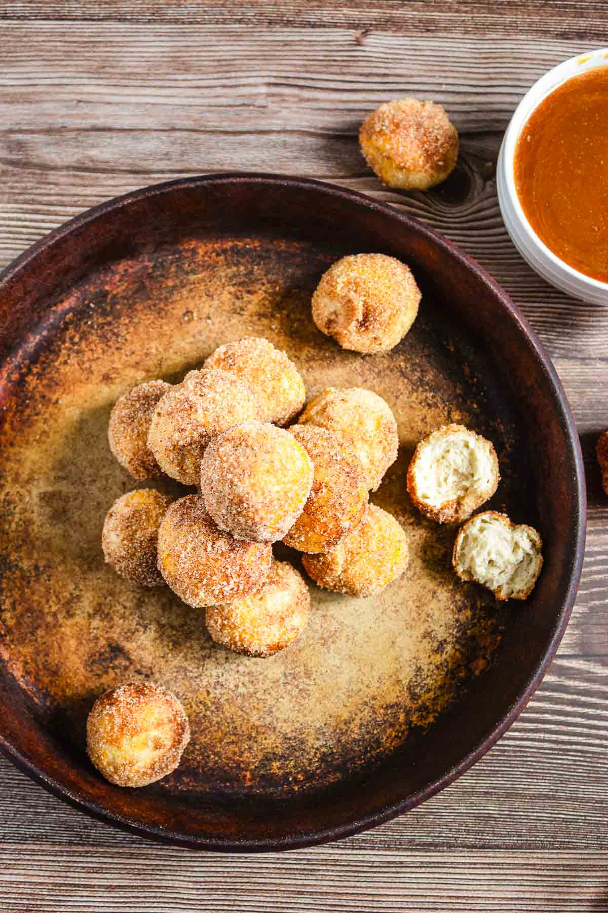 A pile of cinnamon sugar donut holes on a plate with a bowl of caramel sauce on the side.
