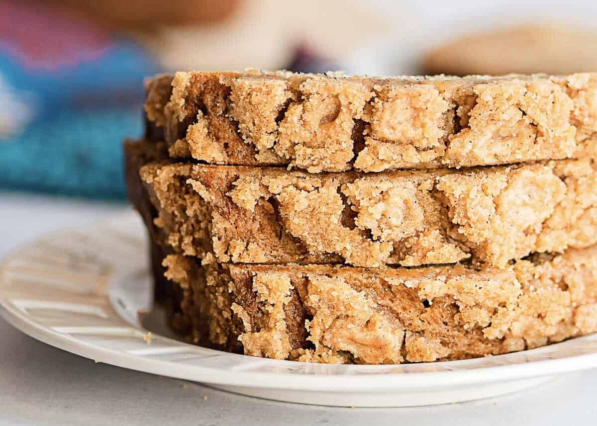 Three slices of banana bread with a golden streusel topping are stacked on a white plate, seen up close.