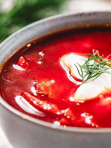 A bowl of borscht soup with sour cream and dill garnish, with a spoon in the bowl.