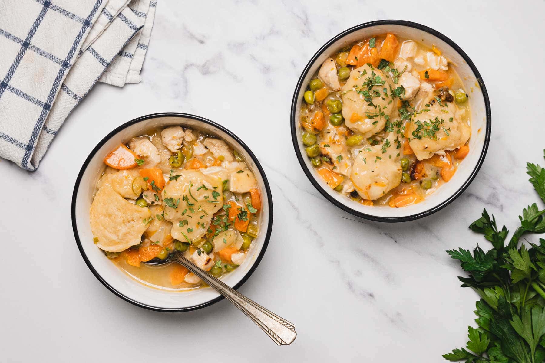 Two bowls of creamy easy chicken and dumplings skillet stew with vegetables, garnished with herbs on a marble surface.