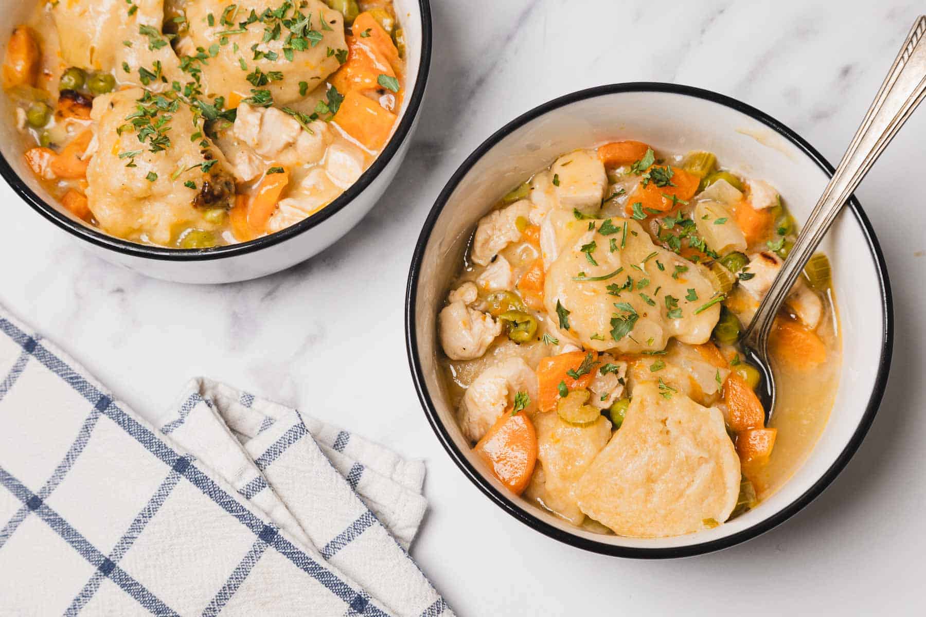 Two bowls of Chicken and Dumplings with vegetables, garnished with herbs, sit on a marble surface with a napkin—perfect for fans of easy chicken recipes.