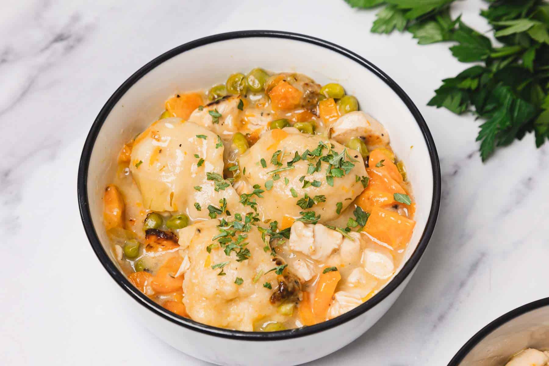 A comforting bowl of easy chicken and dumplings skillet features savory chicken and vegetable stew, topped with fluffy dumplings and a sprinkle of chopped parsley.