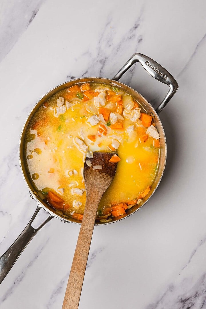 A pot of soup with carrots, onions, and broth, stirred with a wooden spoon on a marble countertop—perfect inspiration for easy skillet chicken recipes or classic chicken and dumplings.