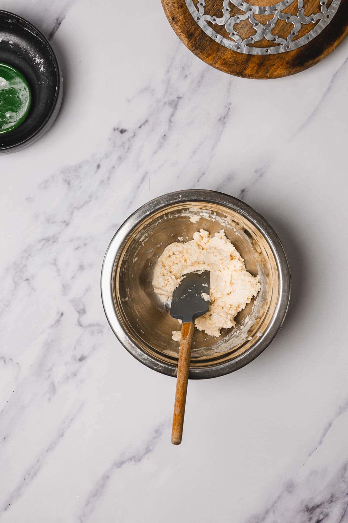 A metal bowl with a spatula and creamed mixture on a marble surface hints at an Easy Chicken Recipe; plate, tray, and skillet nearby set the scene for comforting classics like Chicken and Dumplings.