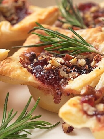 Pastry cups filled with nuts and jam, garnished with fresh rosemary on a white plate.