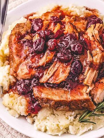 Shredded pork with cranberry sauce served over mashed potatoes, garnished with rosemary on a white plate.