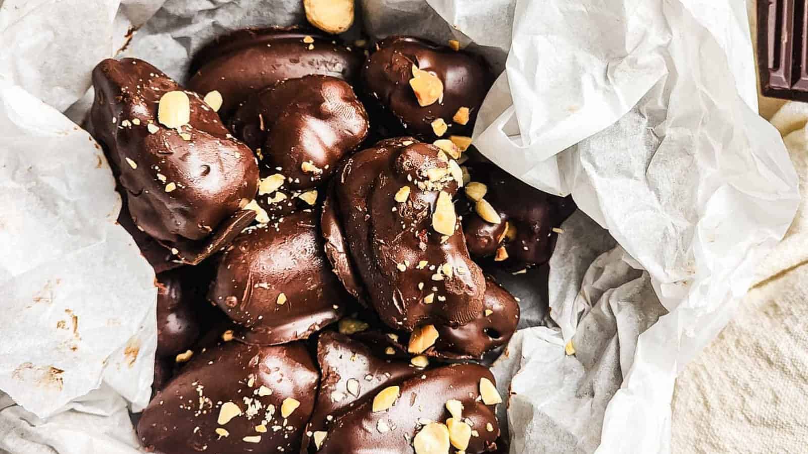 Chocolate-covered candies with a peanut butter filling, topped with crushed nuts, in a box lined with parchment paper.