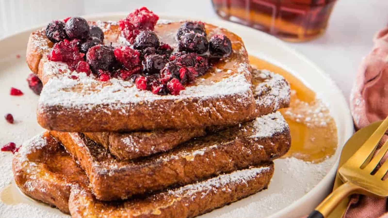Two slices of French toast on a white plate with a brown rim, being cut with a fork and knife.