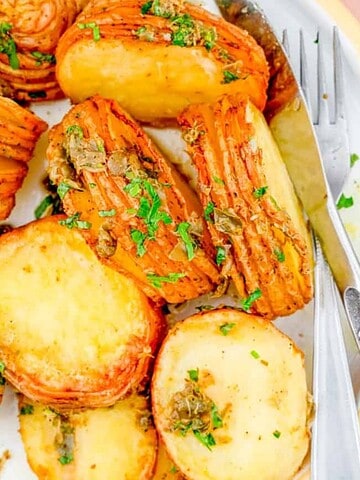 Sliced roasted potatoes garnished with herbs on a white plate with a fork and knife.