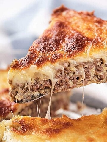 A slice of cheesy, baked meat pie being lifted from a glass dish with a spatula.