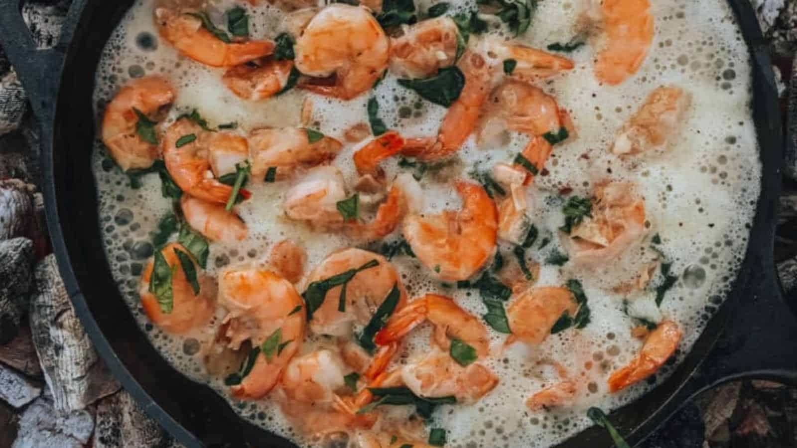 Shrimp cooking in a skillet with bubbling sauce and fresh herbs on top.