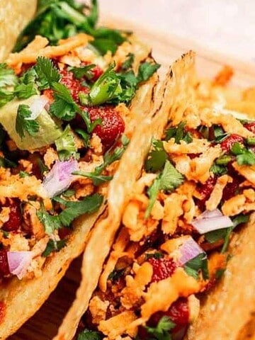 Three loaded tacos with crispy shells, fresh cilantro, onions, and shredded filling, with lime wedges and salsa.