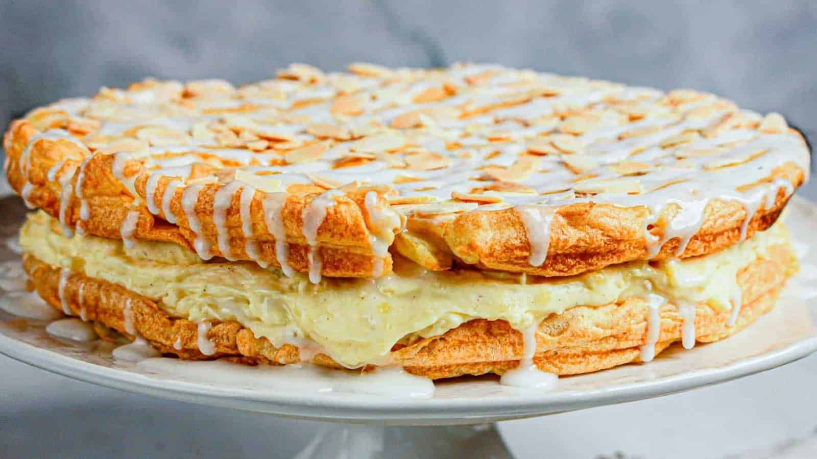 A layered almond pastry cake with cream filling, drizzled with white icing and topped with sliced almonds.