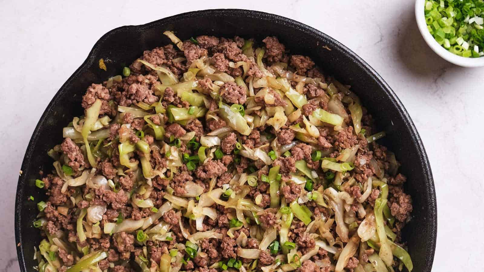 Ground beef and cabbage stir fry being scooped out from a skillet.