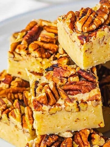 Squares of pecan-topped fudge stacked on a white plate.