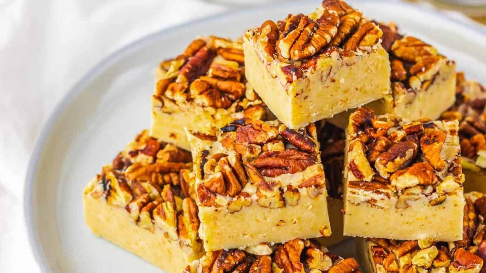 A plate of pecan-topped dessert bars stacked on a white plate, set on a woven placemat.