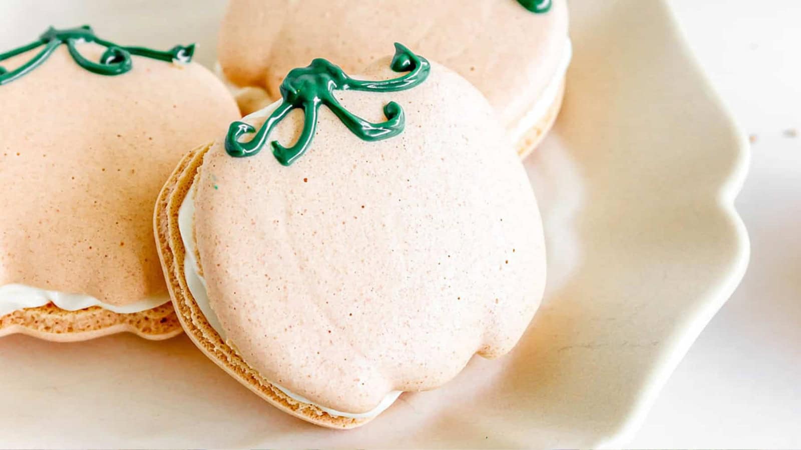 Pumpkin-shaped macarons with green icing stems on a white plate.