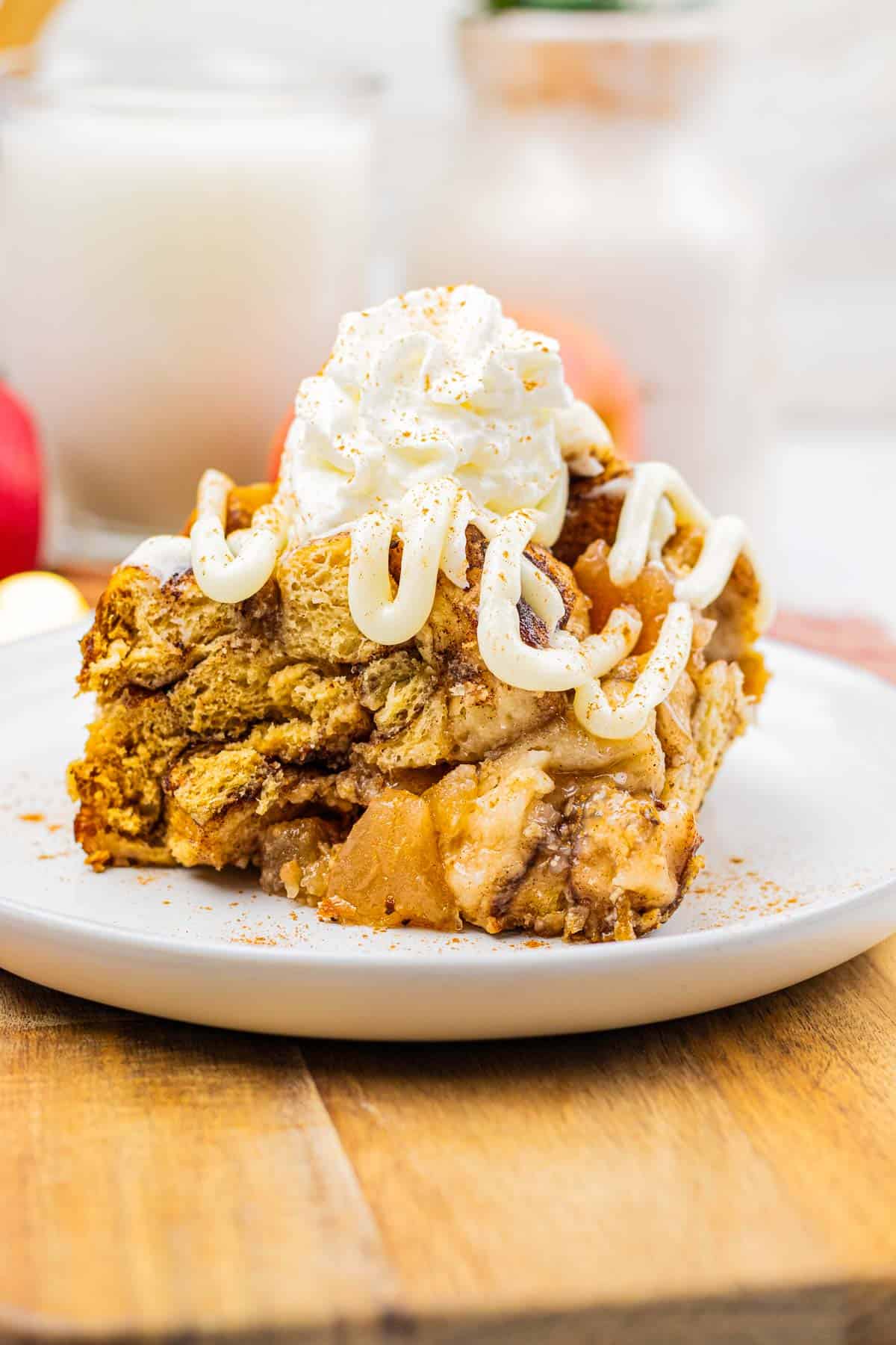 A slice of apple bread pudding, inspired by slow cooker apple pie cinnamon roll casserole, topped with whipped cream and icing on a white plate.