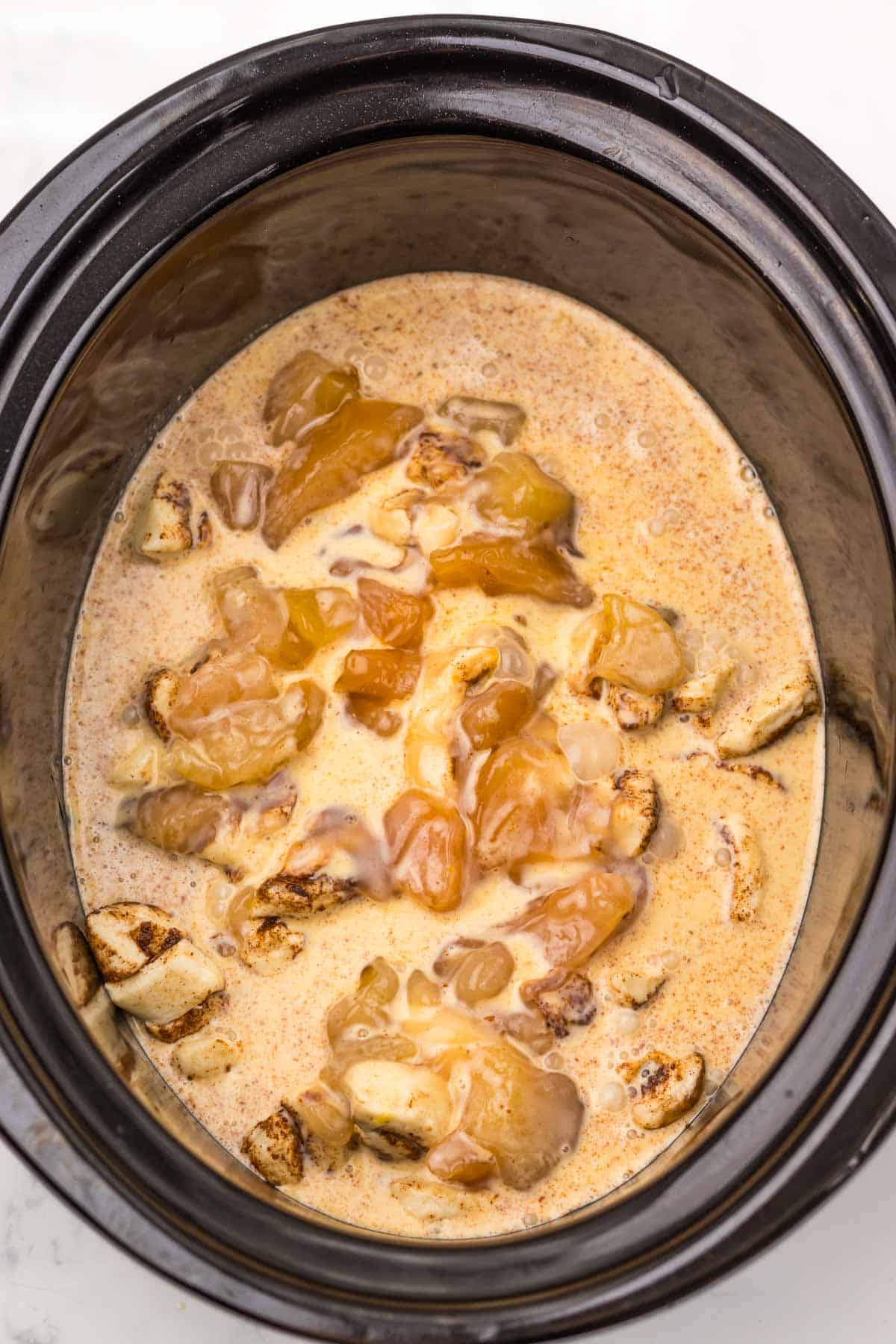 A slow cooker apple pie cinnamon roll casserole filled with chunks of cinnamon rolls, apple pie filling, and creamy sauce.