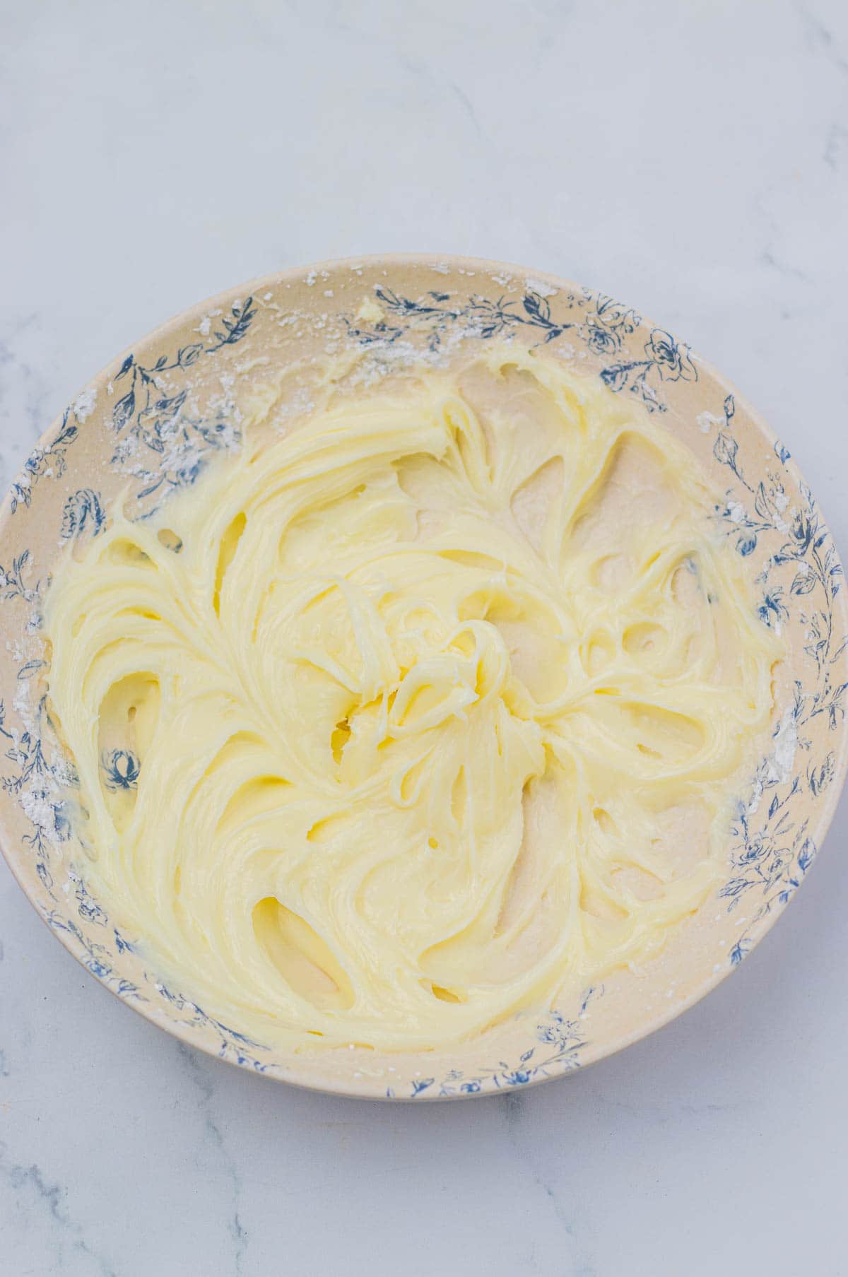 A bowl with creamy yellow buttercream frosting on a light surface, perfect for topping a slow cooker apple pie cinnamon roll casserole.