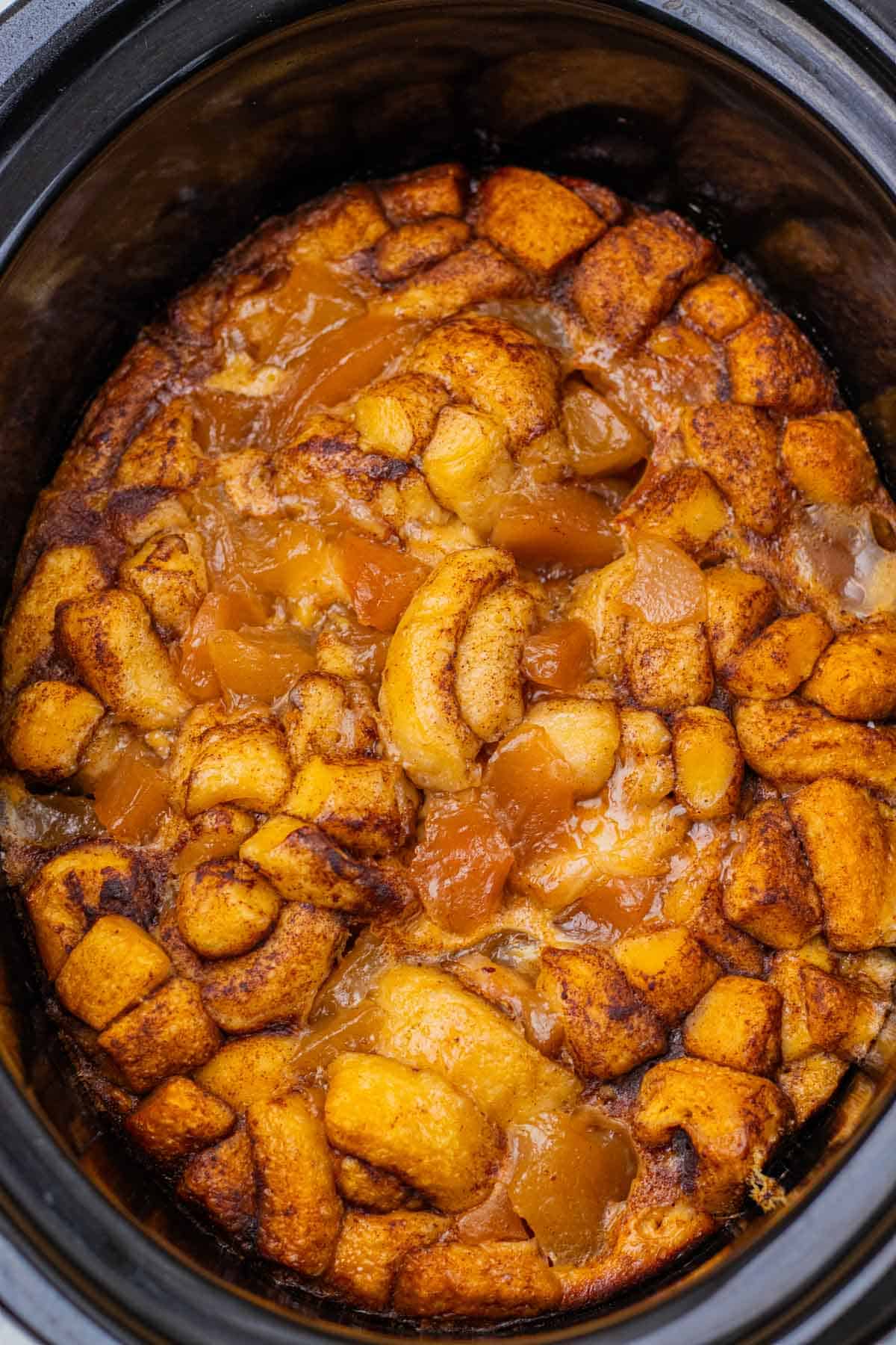 Close-up of a slow cooker apple pie cinnamon roll casserole, featuring a golden biscuit topping and warm cinnamon apples.