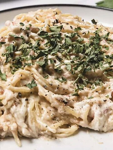 Creamy spaghetti with shredded chicken and herbs on a white plate, garnished with chopped parsley.