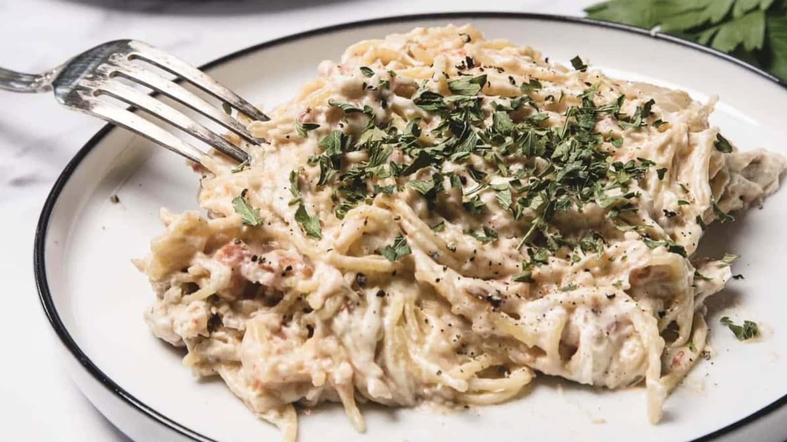 A plate of creamy spaghetti with shredded chicken, topped with chopped parsley and black pepper.