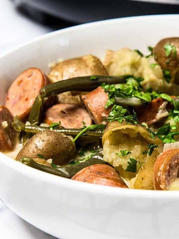 A bowl of sausage, potatoes, and green beans garnished with chopped parsley.