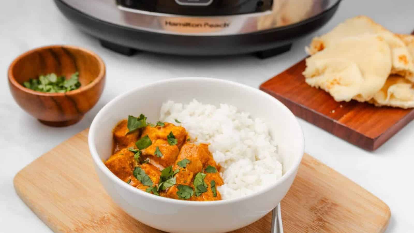 An overhead image of slow cooker tikka masala in a bowl with rice, with a slow cooker on the background.