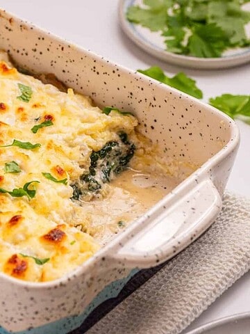 Baked casserole with a golden cheese topping and sprinkled herbs in a white dish on a cloth.