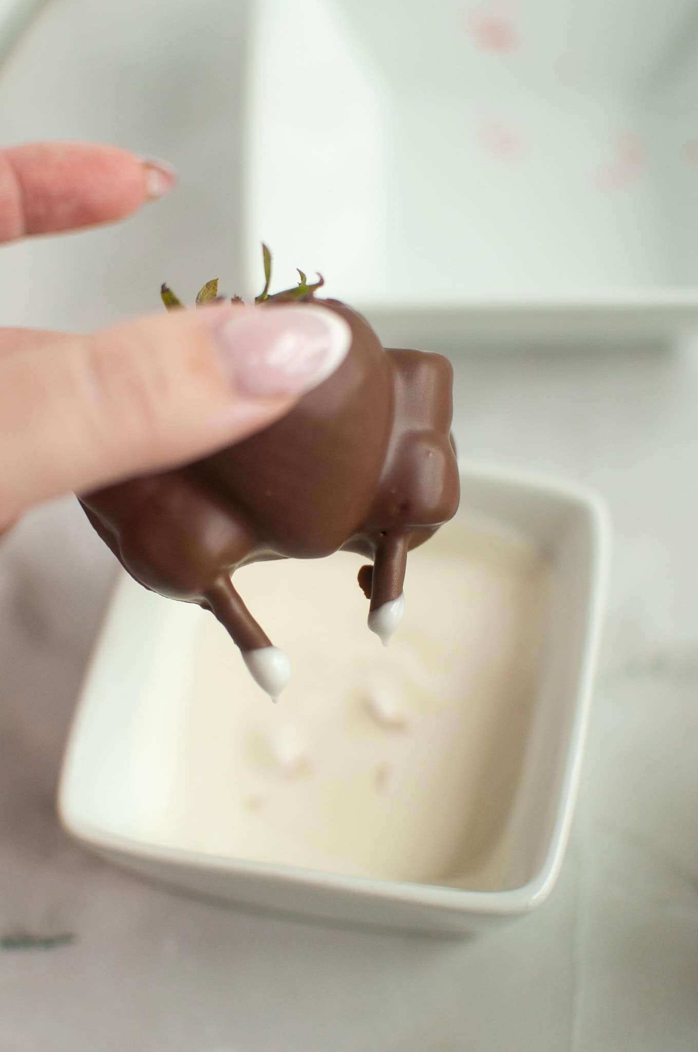 Hand holding a Chocolate Covered Strawberry Turkey above a bowl of white sauce, ready to dip&mdash;perfect for your Thanksgiving celebration.