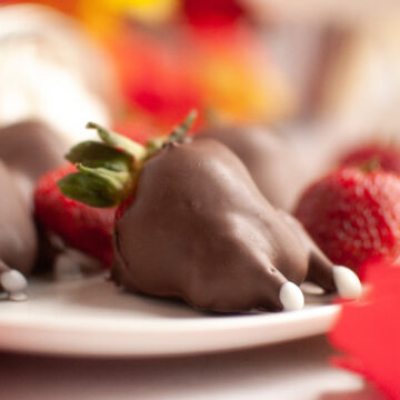 Chocolate-covered strawberries decorated to look like mice, with white candy tails and ears, on a white plate.