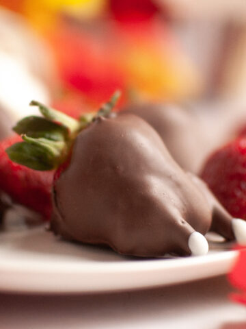 Chocolate-covered strawberries decorated to look like mice, with white candy tails and ears, on a white plate.