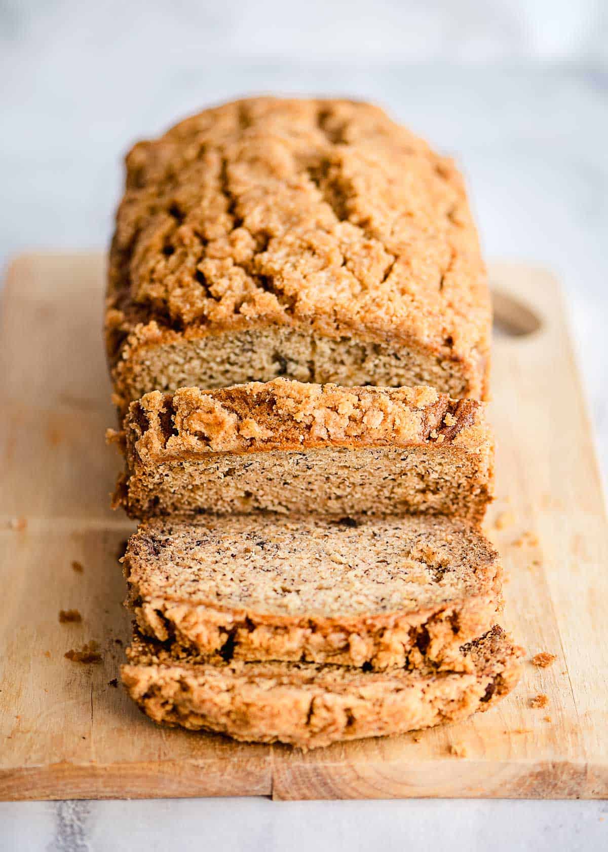 Sliced loaf of banana bread with streusel topping on a wooden cutting board.