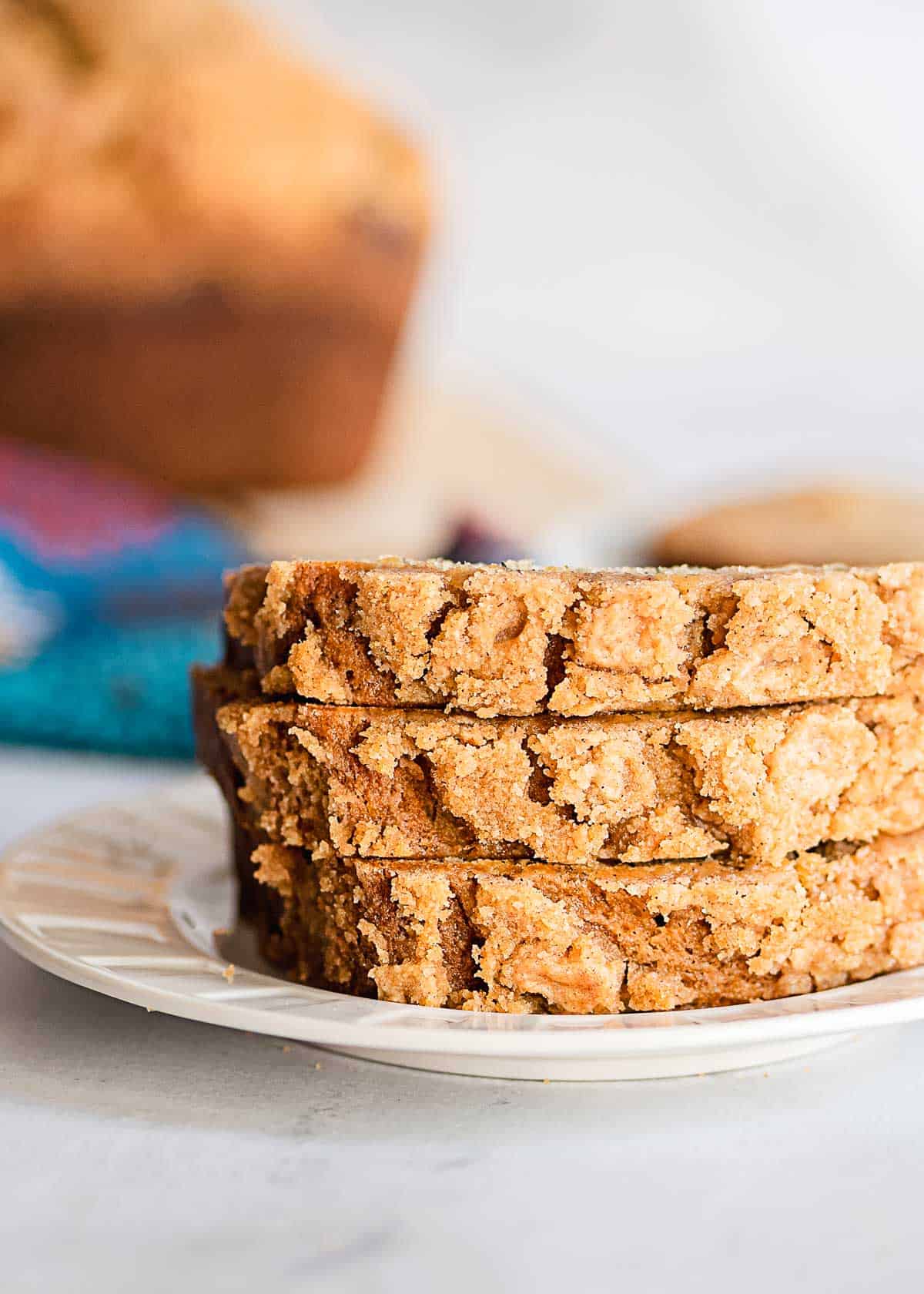 Three slices of crumbly, golden brown banana bread with a sweet streusel topping are stacked on a white plate.