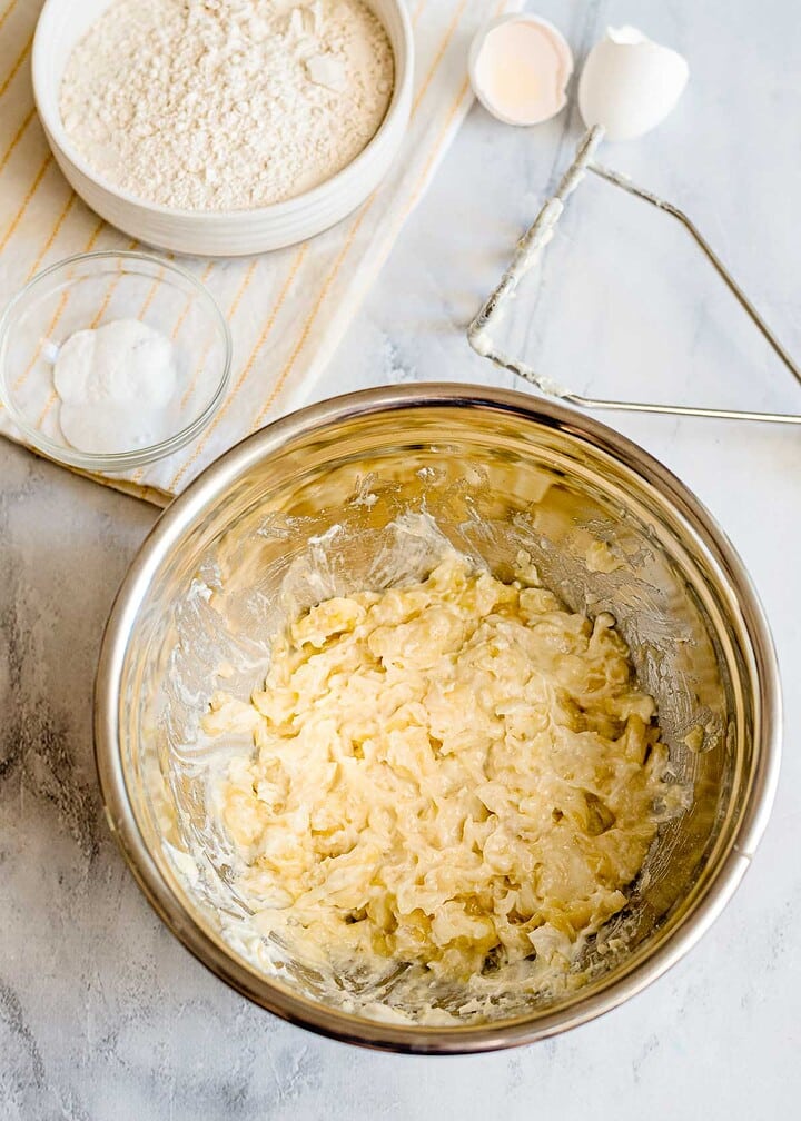 A mixing bowl with creamed butter and sugar, next to flour, baking powder, and a cracked egg on a counter—perfect for starting your favorite Banana Bread Recipe or adding a sweet streusel topping.