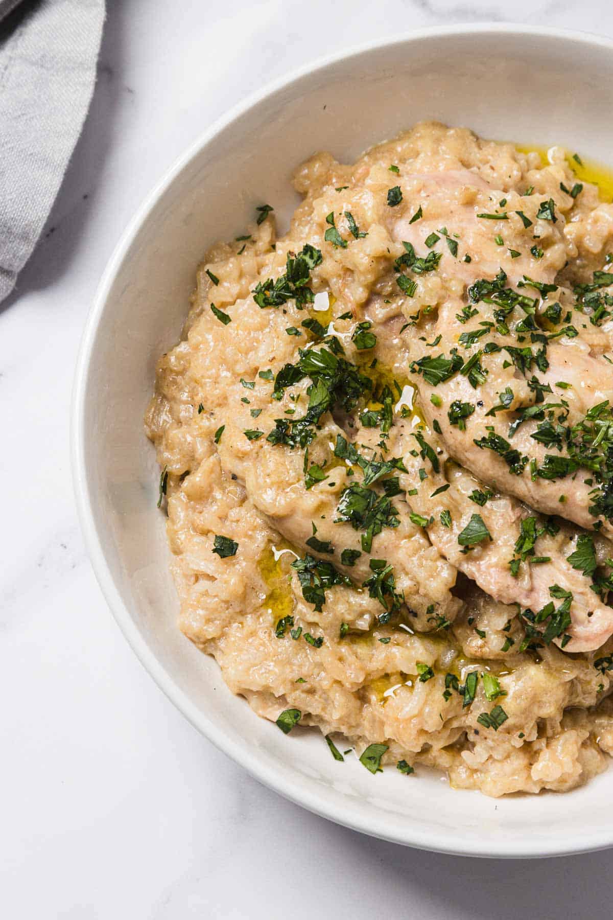 Creamy crockpot chicken and rice garnished with chopped parsley in a white bowl on a marble surface.