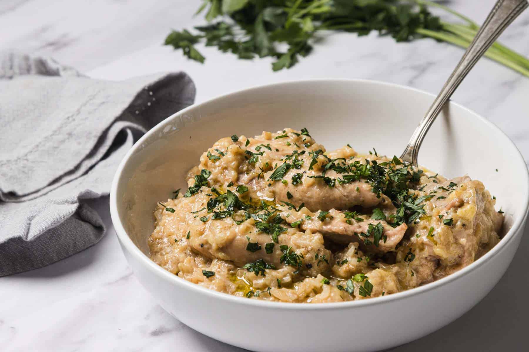 A bowl of creamy chicken stew garnished with chopped herbs, with a spoon and a cloth napkin nearby.