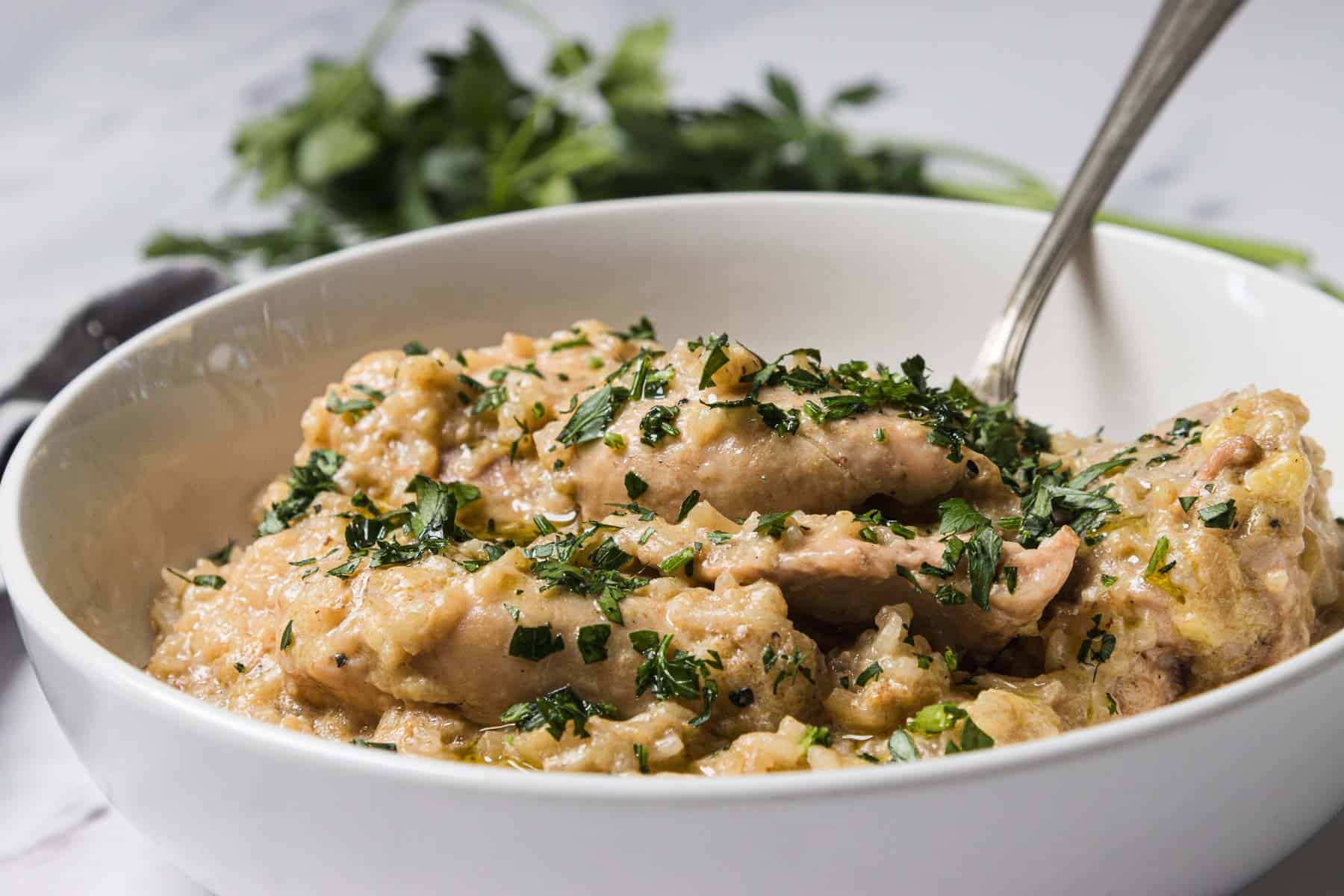 A bowl of creamy Crockpot chicken stew topped with chopped herbs, with a spoon and fresh parsley in the background—a comforting favorite among crockpot recipes.
