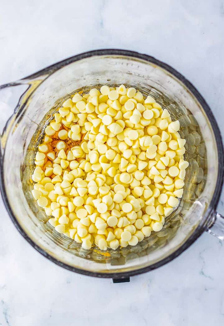 White chocolate chips in a glass mixing bowl, ready to be melted on a marble countertop for a delicious Pecan Pie Fudge recipe.
