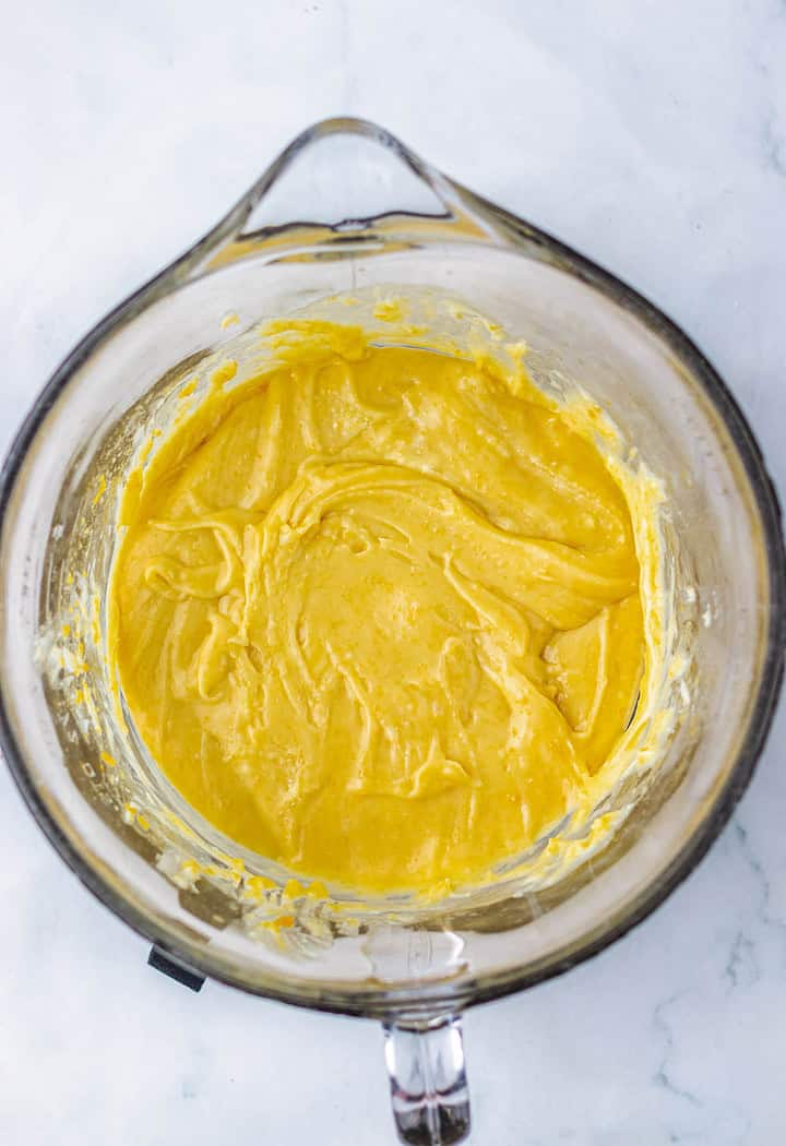 A glass mixing bowl filled with thick, yellow batter on a white surface, perfect for creating a rich pecan pie fudge recipe.