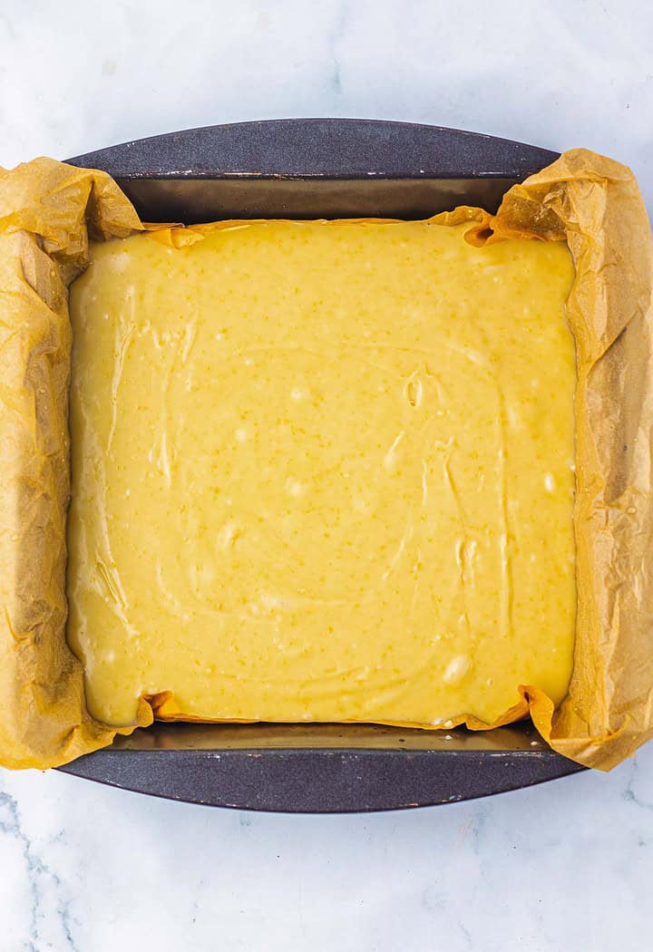 A baking pan lined with parchment paper filled with smooth yellow cake batter, ready to be baked into a delicious treat inspired by classic pecan pie fudge.