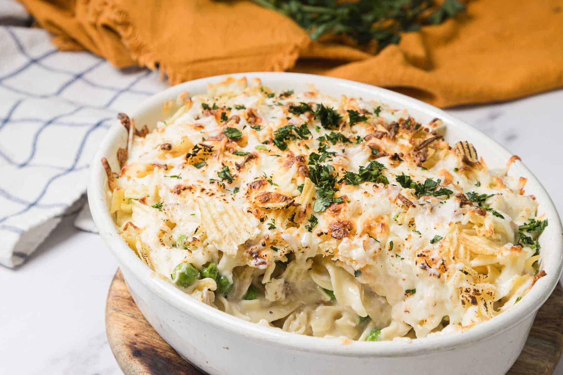 Baked casserole recipe topped with melted cheese and herbs in a white dish on a wooden board, perfect for fans of classic tuna casserole.