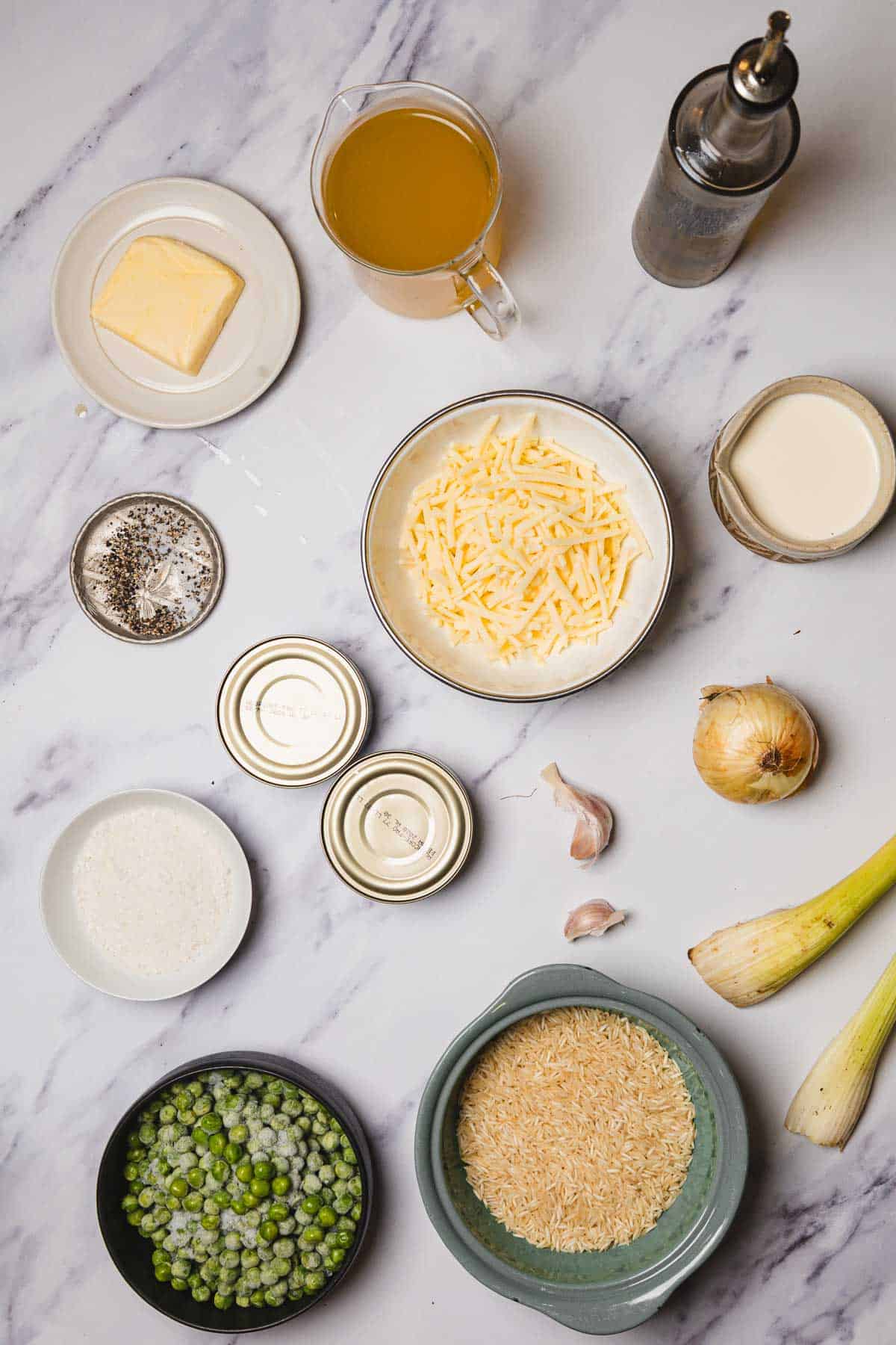 Ingredients for a casserole recipe laid out on a white surface, including pasta, tuna, cheese, butter, peas, broth, and seasonings.