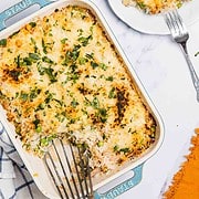 A baked Tuna Casserole topped with melted cheese and herbs, with a serving on a white plate beside it.