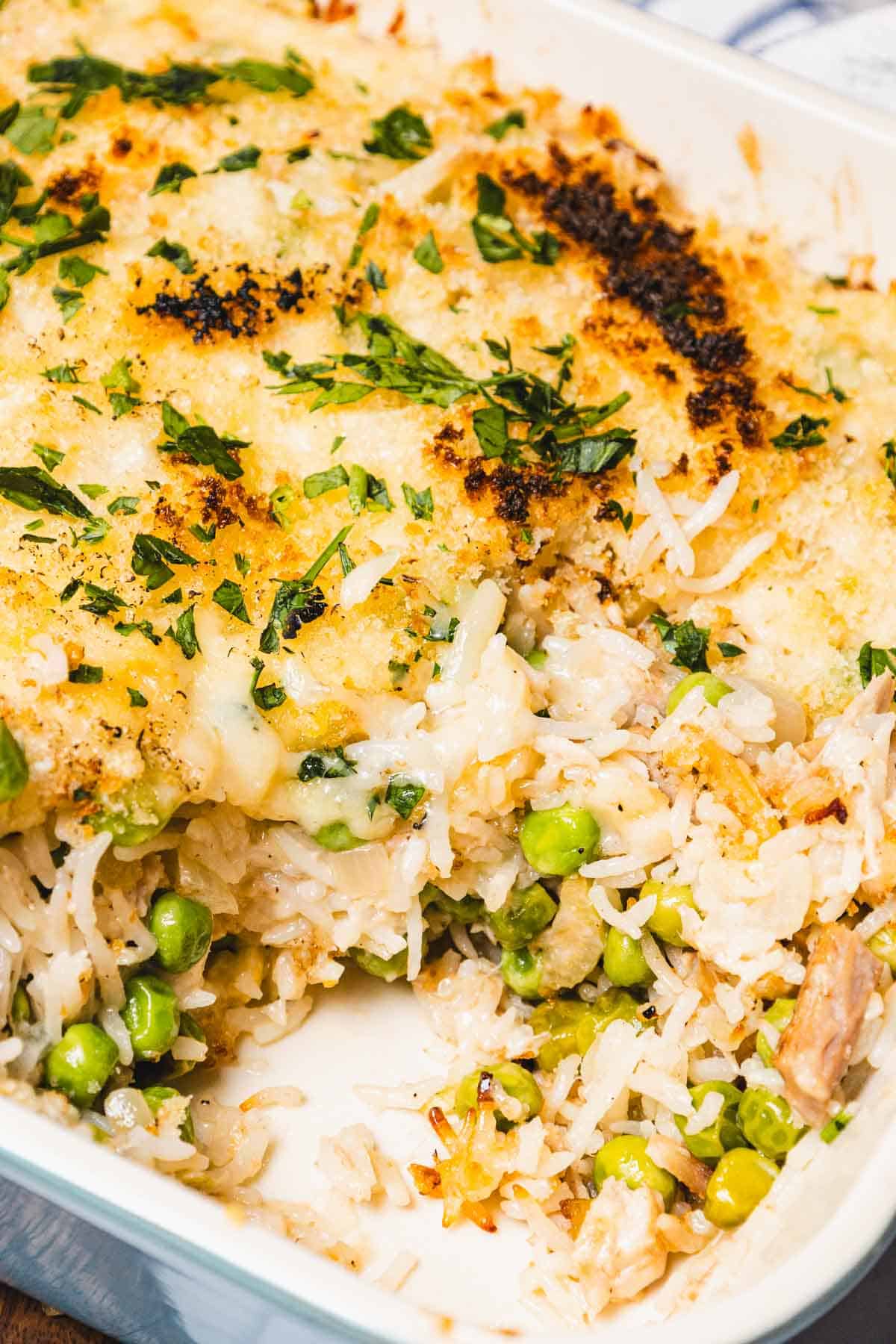 A close-up of a baked rice casserole with peas, shredded tuna, and a golden, crispy breadcrumb topping.