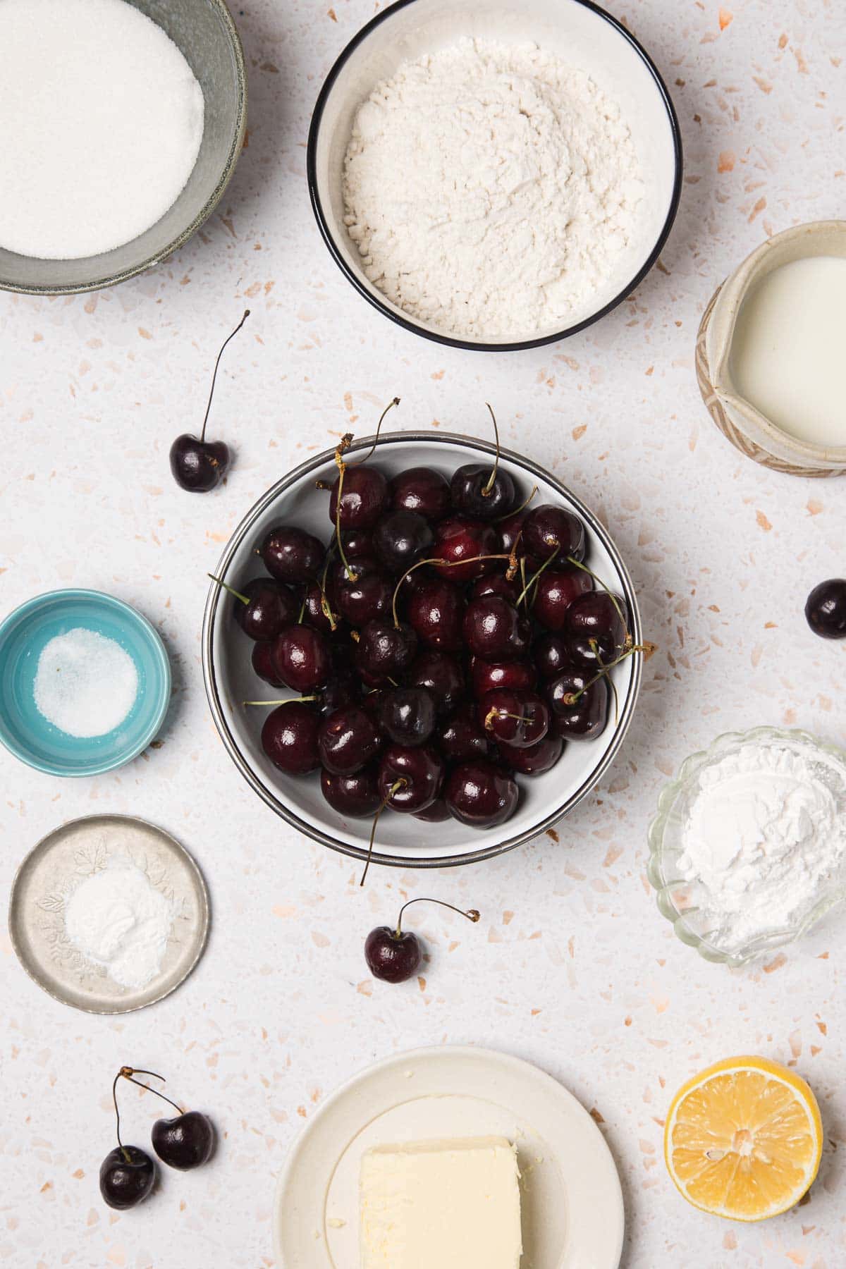 A bowl of fresh cherries surrounded by baking ingredients on a white surface, perfect for whipping up an easy cherry pie.