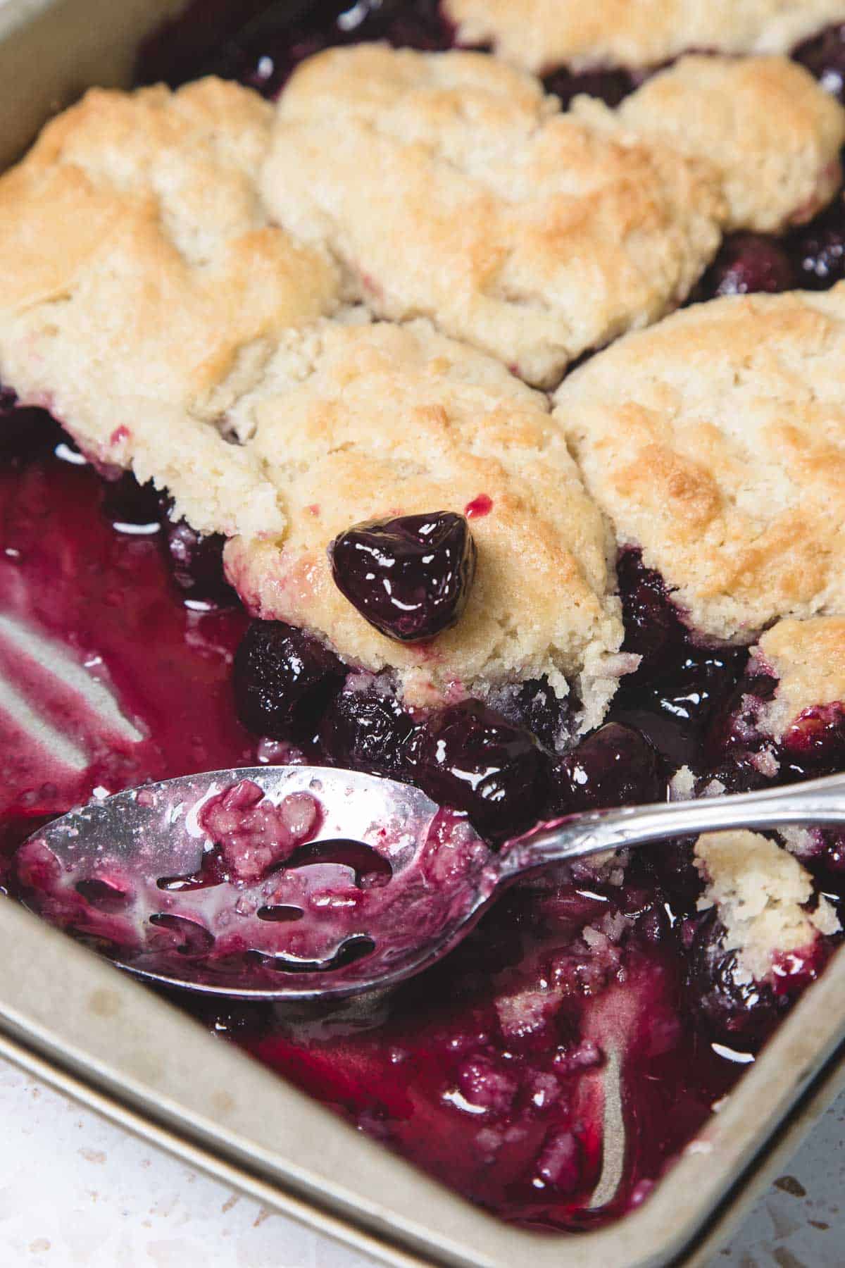 A close-up of an Easy Cherry Pie cobbler with a spoon and biscuit topping in a baking dish.